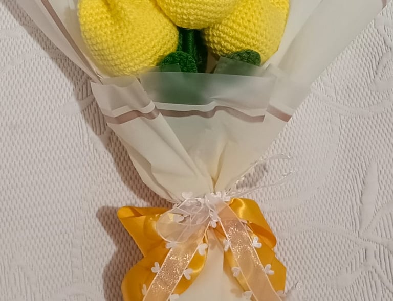 Handmade bouquet of yellow crochet tulips wrapped in white paper with a decorative ribbon bow.