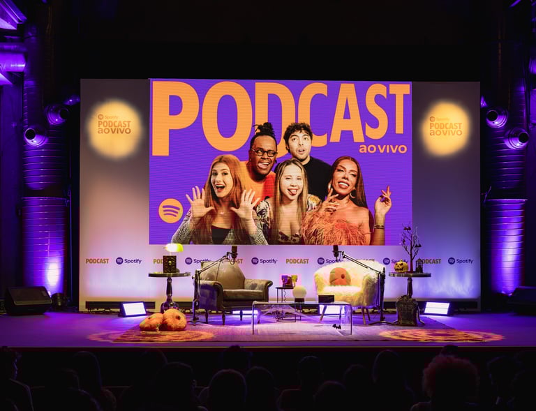 A live Spotify podcast stage with hosts on a large screen and chairs for a live recording event.