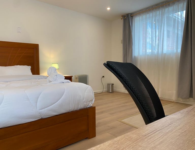 Dormitorio moderno con cama de madera, sábanas blancas y silla de oficina ergonómica para trabajar