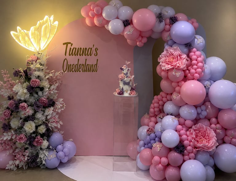 Elegant pink and purple 'Tianna's Onederland' first birthday party decoration with balloon arch, floral arrangements, and a