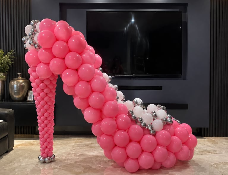 Giant pink and silver balloon high heel sculpture, a decorative party centerpiece in a modern living room.