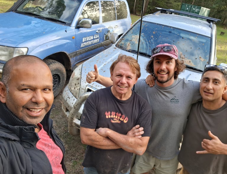 A group of four men posing for a selfie after a Byron 4x4 adventures off-roading trip with muddy SUVs.