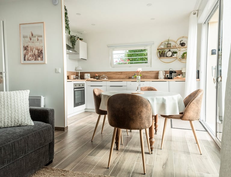 Modern open plan studio apartment featuring a white kitchen, dining table with brown chairs, and cozy living area.