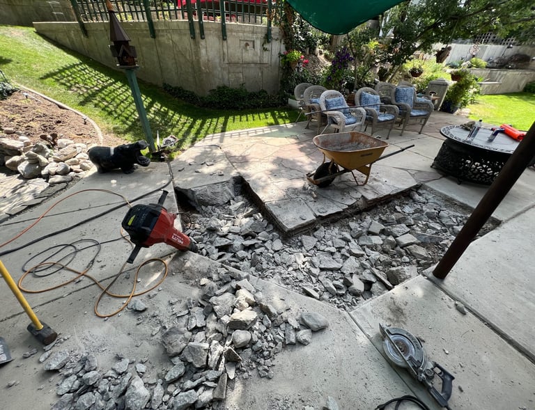 A jack hammer leaning against the side of a patio with concrete that was recently broken up