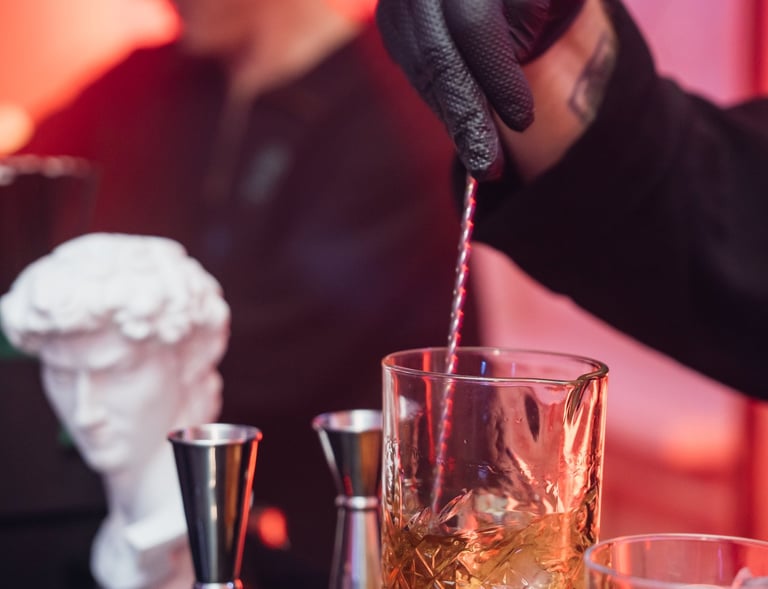Stilingai apšviestame renginyje barmenas maišo kokteilį stiklinėje, naudojant baro šaukštą