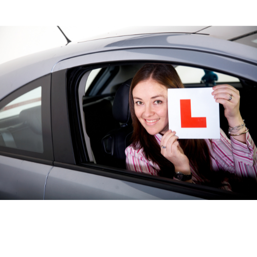 a woman holding up a L red sign for her car. starting her car leaning expirance with let's pass 1st.