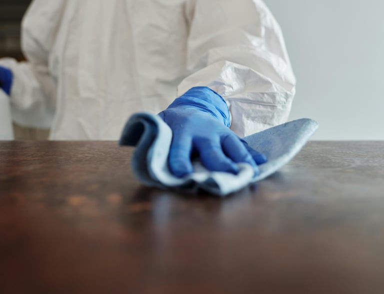 a person in a white lab coat and gloves cleaning a table
