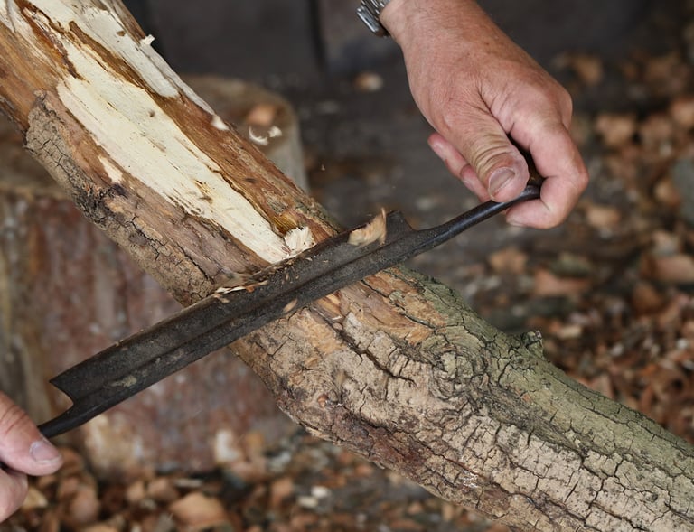 a person holding a drawknife in their hands carving bark from a branch