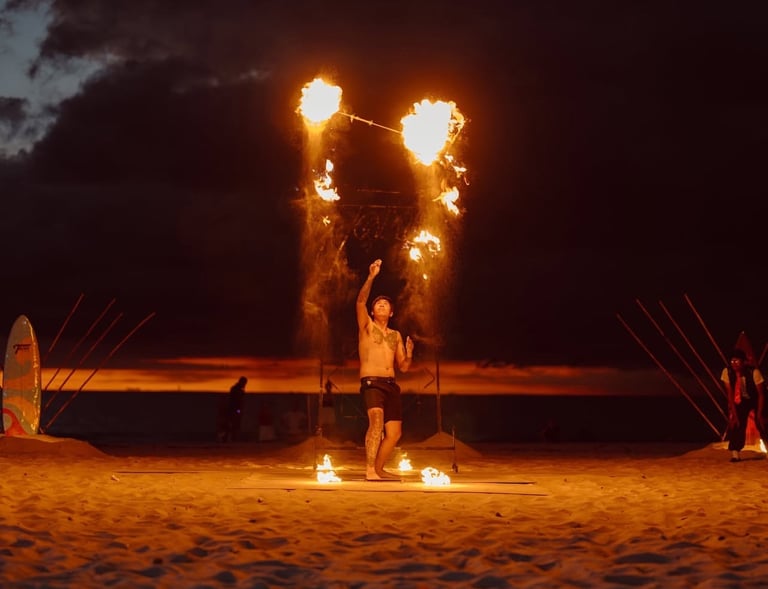 a man throws flaming torches in the air on a beach in Bang Tao Thailand