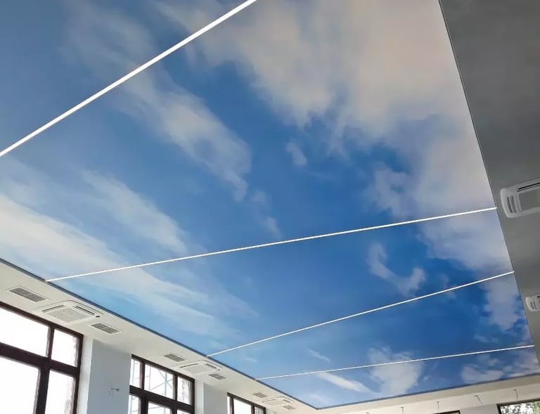 Backlit stretch ceiling with a blue sky and white cloud printed design and linear LED lighting.