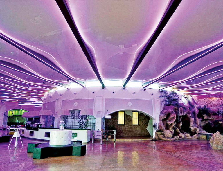 Modern lounge interior featuring wavy purple LED ceiling lighting and artificial rock formations.