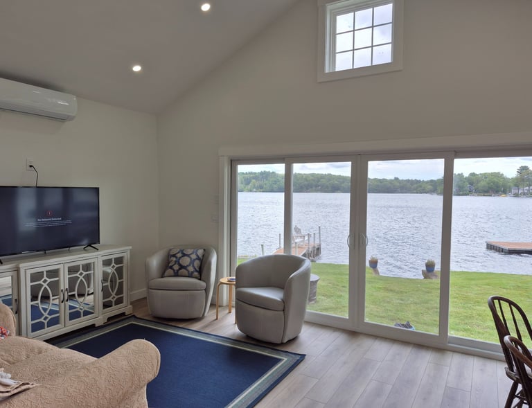 Modern lakefront living room featuring grey swivel chairs and a scenic waterfront view through sliding glass doors.