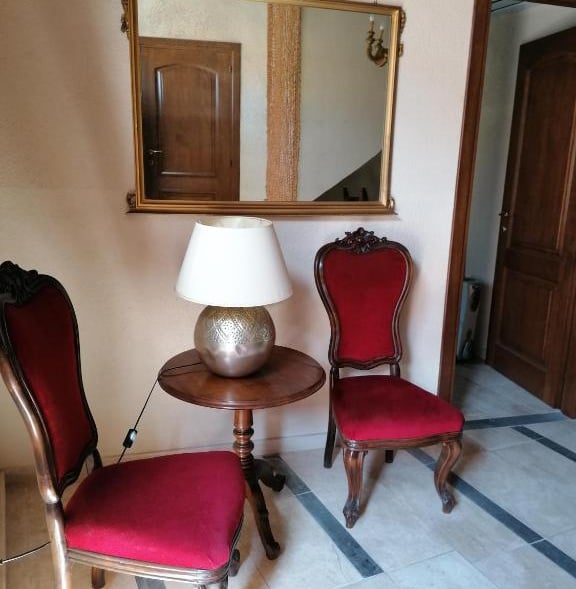 Antique red velvet chairs and a wooden side table with a lamp in a classic foyer with a large gold mirror.