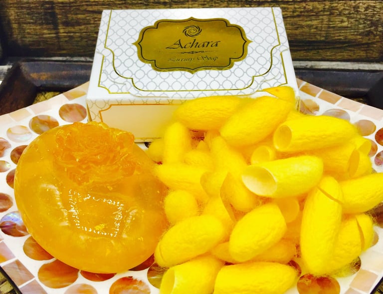 Handmade Achara luxury silk soap bar next to yellow silkworm cocoons on a mosaic plate.