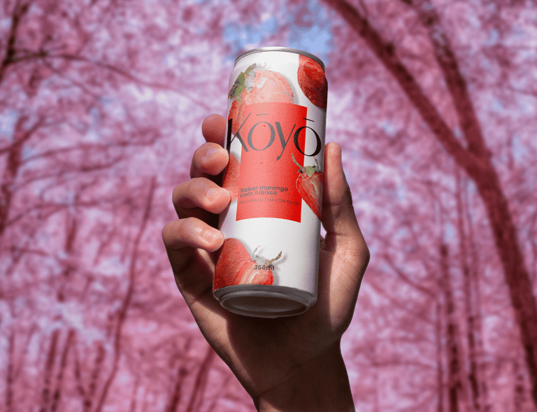 Lata da bebida Koyō sabor morango sendo segurada por uma mão, com fundo rosa de árvores floridas, tr