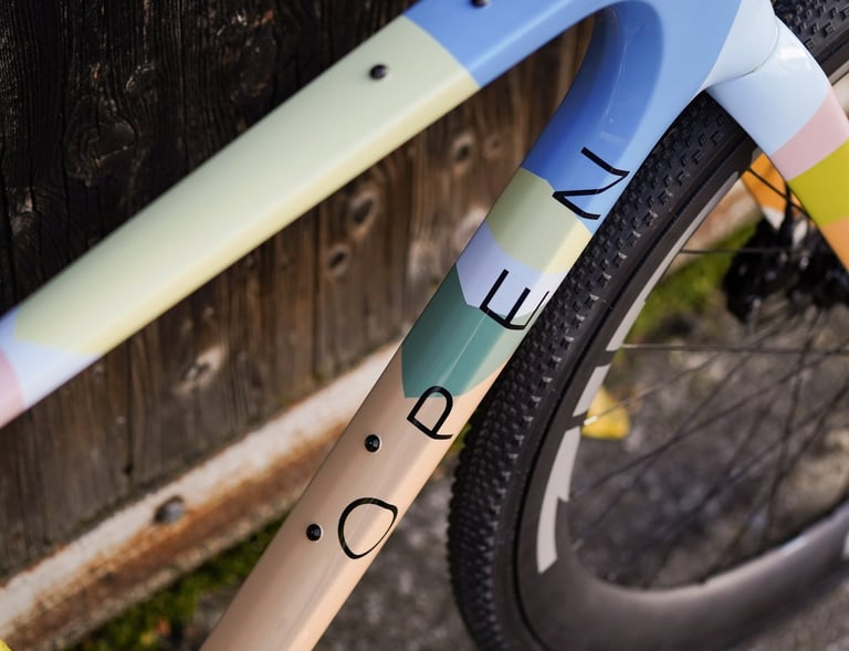 Close-up of a custom painted Open gravel bike frame with pastel color blocking and carbon wheels.