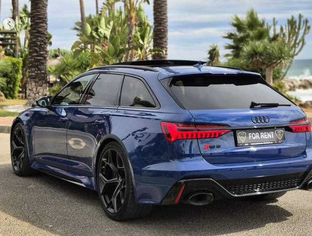Blue Audi RS6 Avant luxury rental car parked on a tropical coastal road with palm trees.