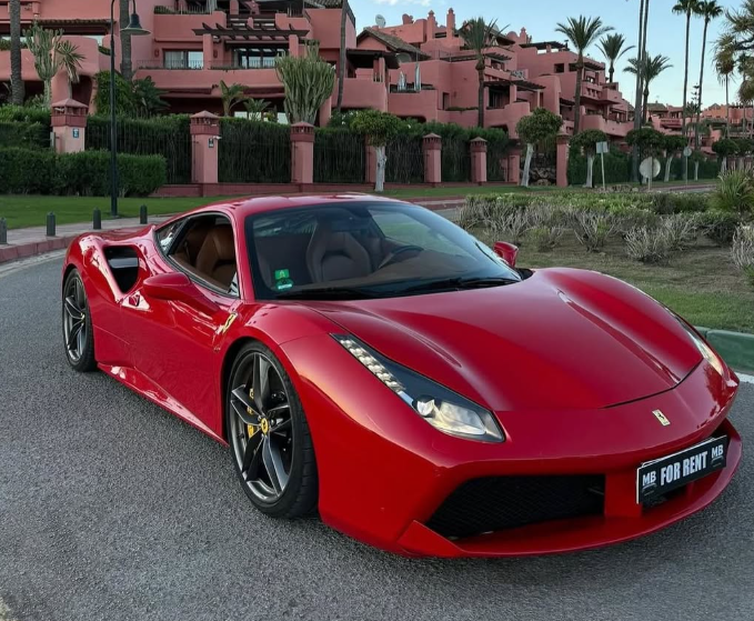 Red Ferrari 488 luxury sports car for rent parked on a street near Mediterranean villas.