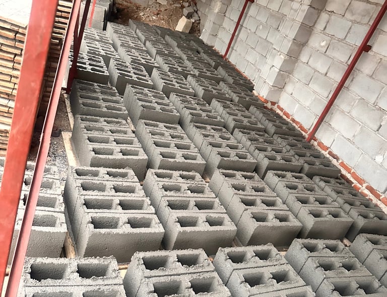 Rows of grey concrete hollow blocks stored in a warehouse for building and construction projects.