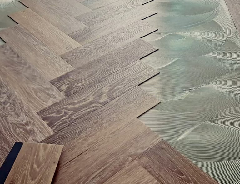 Professional installation of oak herringbone wood flooring onto wet adhesive on a level subfloor.