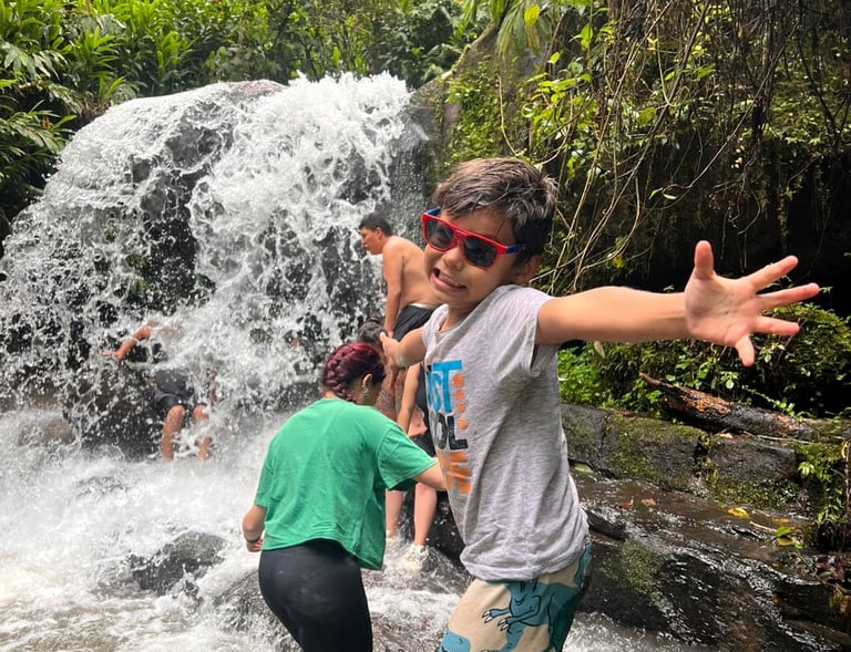 Un niño con gafas de sol posa emocionado frente a una cascada en la selva tropical junto a su famili