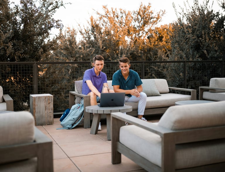 two men sitting on a patio with laptops