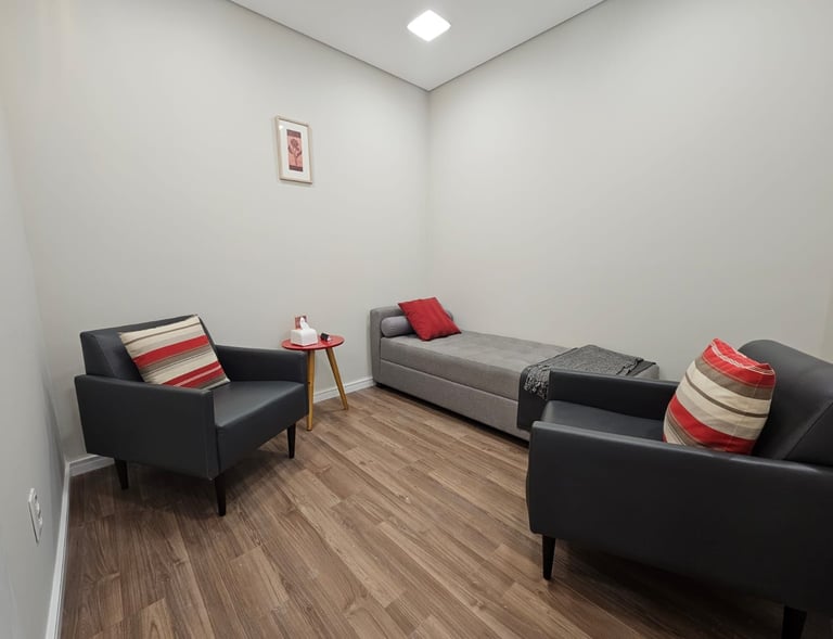 Ambiente de terapia com duas poltronas pretas com almofadas coloridas, uma mesa de madeira clara e j