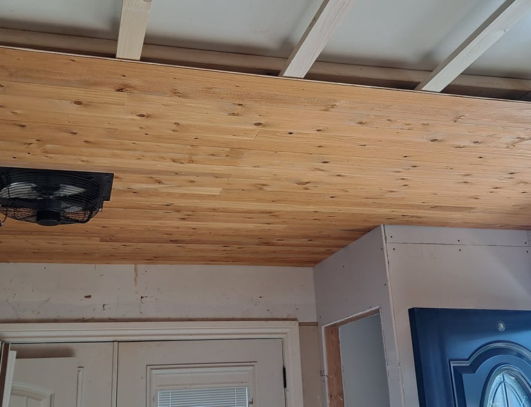 Partially installed wood plank ceiling with integrated ventilation fan in residential entryway levelled renovation project