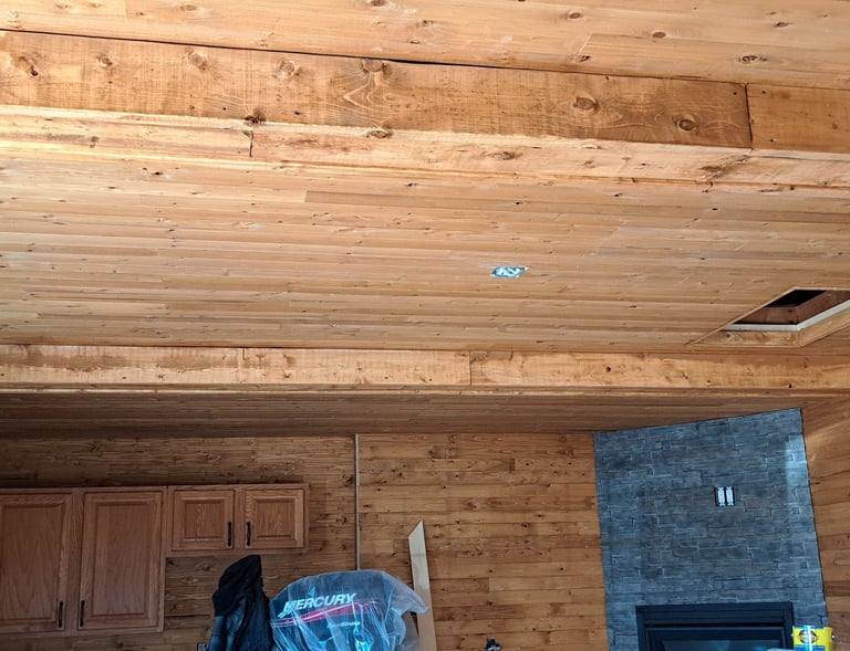 Wood-paneled ceiling with exposed beams and stone accent wall in rustic home interior renovation