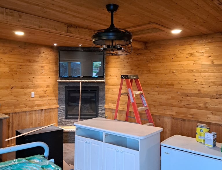 Rustic living room renovation in progress featuring wood-paneled ceiling and walls, stone fireplace, and new cabinetry