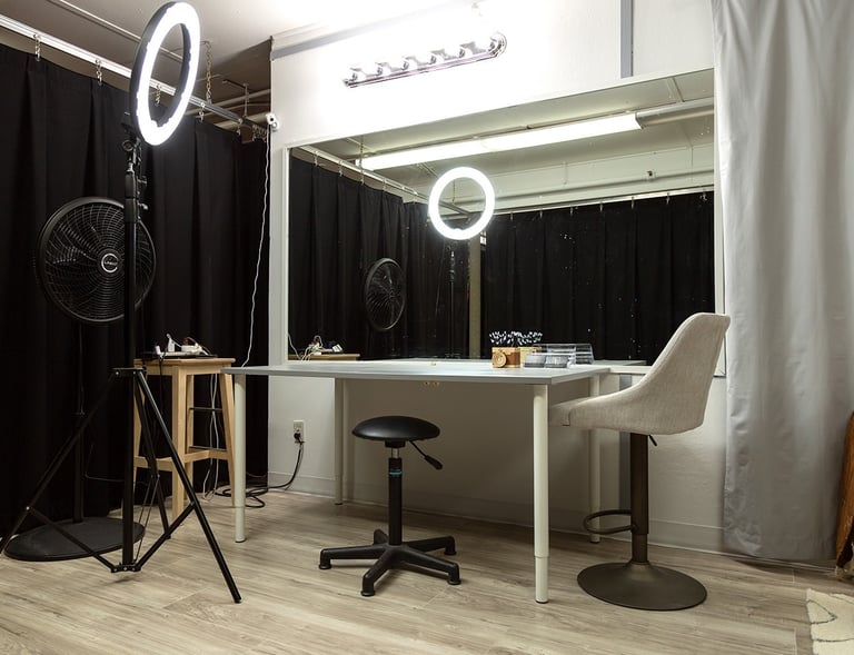 a room with a table and chairs and a fan and large mirror vanity for makeup