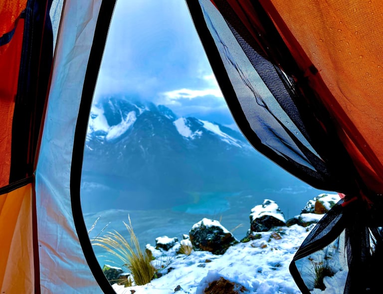 A scenic view of Peruvian snowy mountains and a blue lake through an open orange camping tent door.