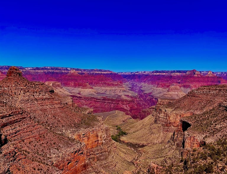 Panoramic view of the Grand Canyon National Park with red rock layers under a clear blue sky.