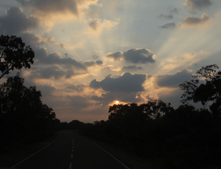 Golden sun rays breaking through clouds over a scenic asphalt highway at sunset.