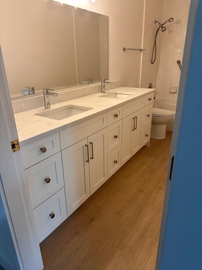 Modern bathroom with double-sink white shaker vanity, quartz countertop, and wood-look flooring — RT
