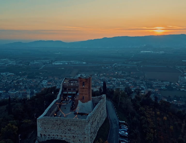Aerial view of a medieval Italian castle at sunset overlooking a scenic valley landscape.
