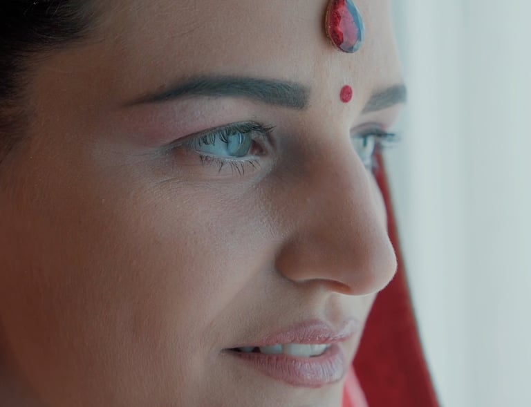 Close-up of a woman wearing traditional Indian bridal makeup with a red bindi and teardrop maang tikka.