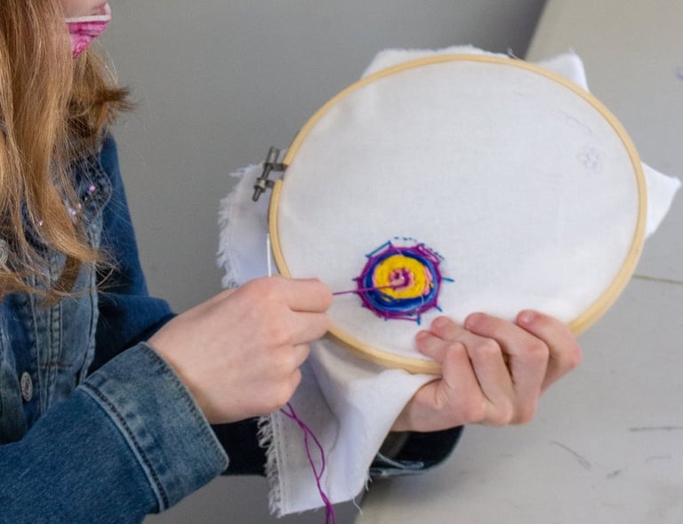 Young girl pulling thread through fabric to create an embroidered spider web.