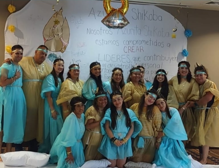 A group of people wearing blue and gold robes posing in front of a white leadership development banner.