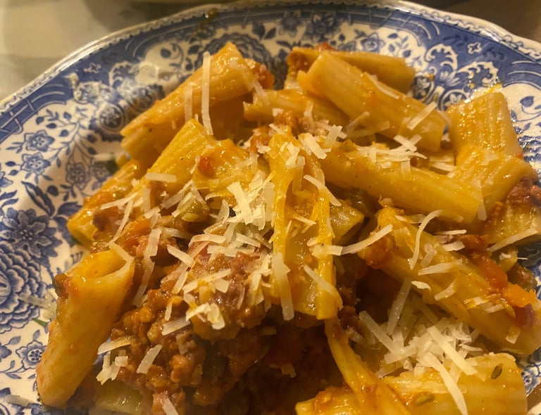 Rigatoni pasta with savory meat bolognese sauce and grated parmesan cheese on a blue floral plate.
