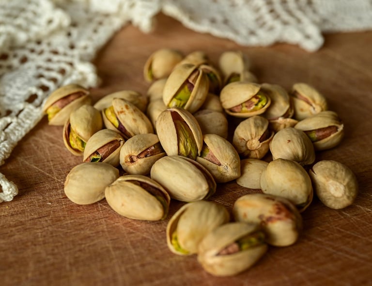 A pile of roasted, salted pistachios in their shells on a rustic wooden table with white lace.