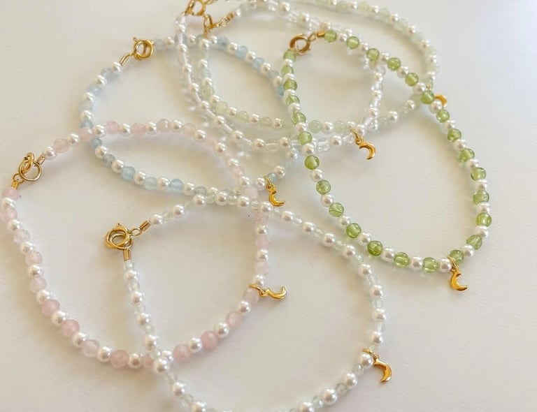 Collares de cuentas hechos a mano con perlas y dijes de luna dorados sobre una superficie blanca.