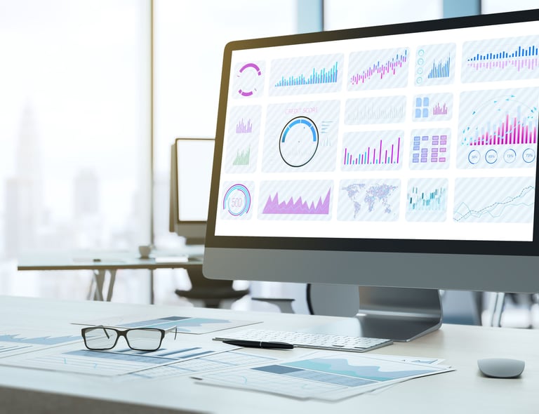 view of an office showing charts and graphs on a computer monitor with printouts, a pen and glasses