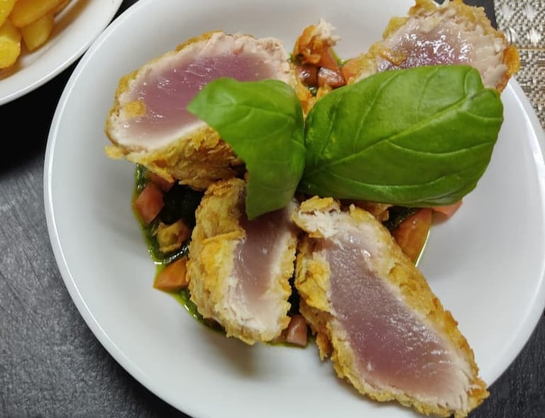 Tagliata di tonno pinna gialla scottata in crosta servita con pomodorini e basilico fresco.