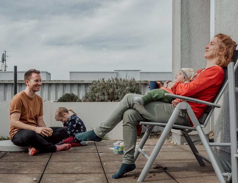 Eine junge Familie entspannt sich an einem sonnigen Tag gemeinsam auf einer  Dachterrasse.