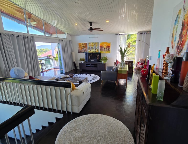 Modern bright living room interior with white vaulted ceilings, sliding balcony doors, and colorful wall art.