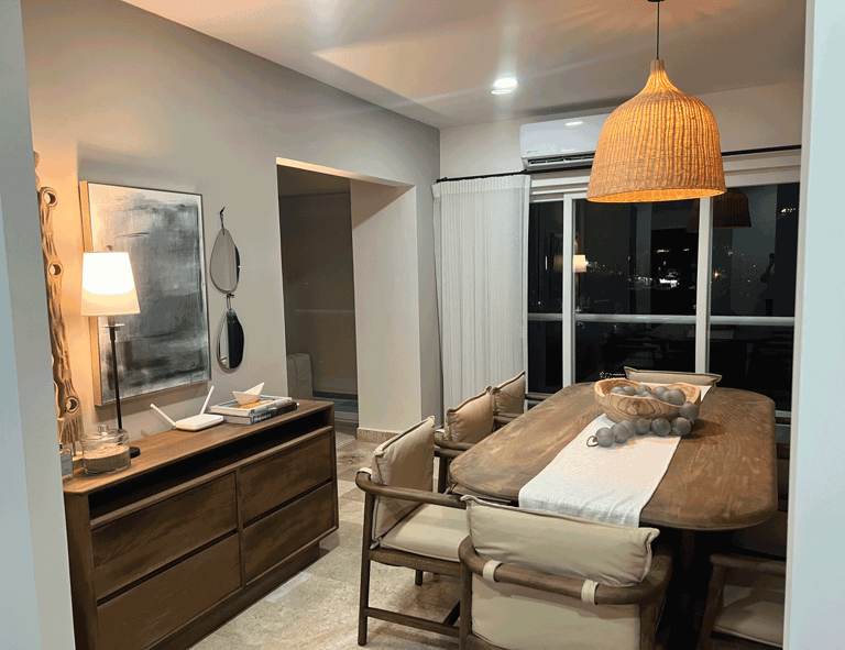 Comedor cálido con mesa de madera, sillas con cojín claro y lámpara colgante de mimbre | KARÄNA