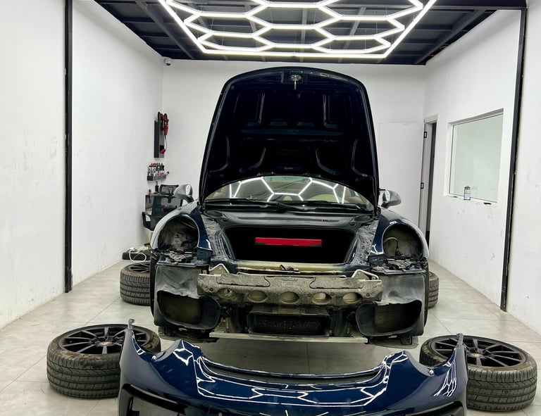A dark blue sports car undergoing professional detailing and repair under hexagonal LED garage lights.