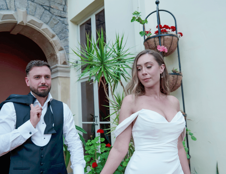 A bride and groom joyfully walking surrounded by floral decorations and smiling guests.