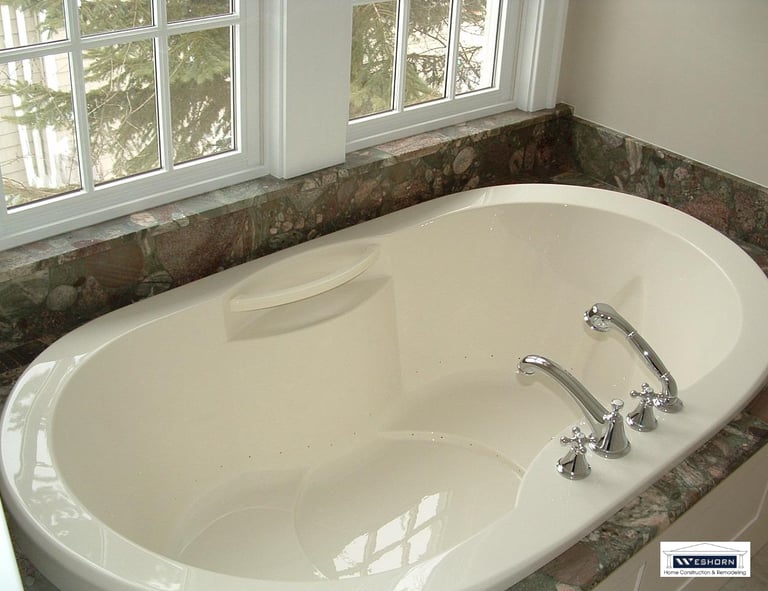 Luxury oval soaking tub with chrome fixtures and granite tile surround in a modern bathroom remodel.
